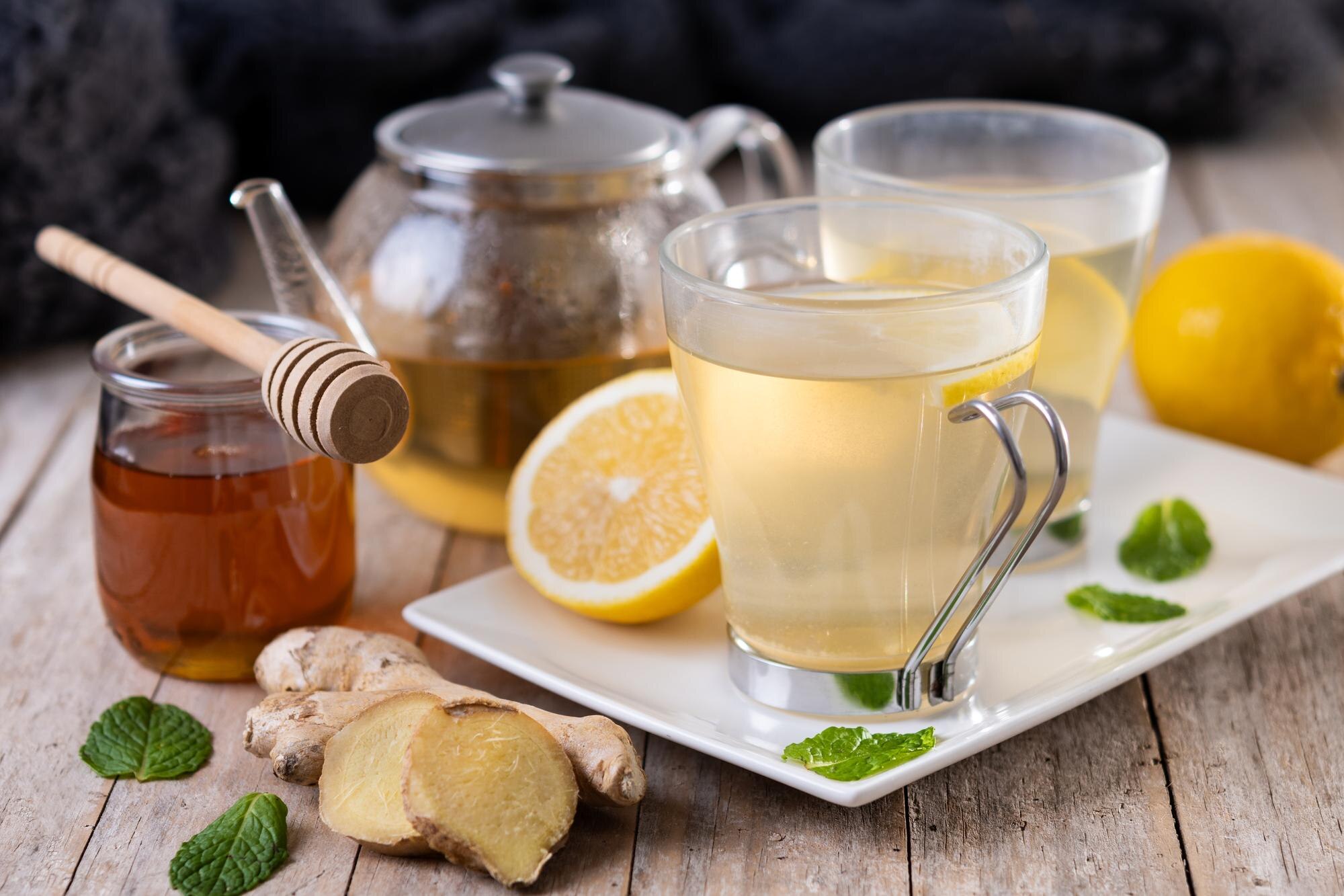 A glass cup of warm ginger and lemon tea with honey on a wooden surface