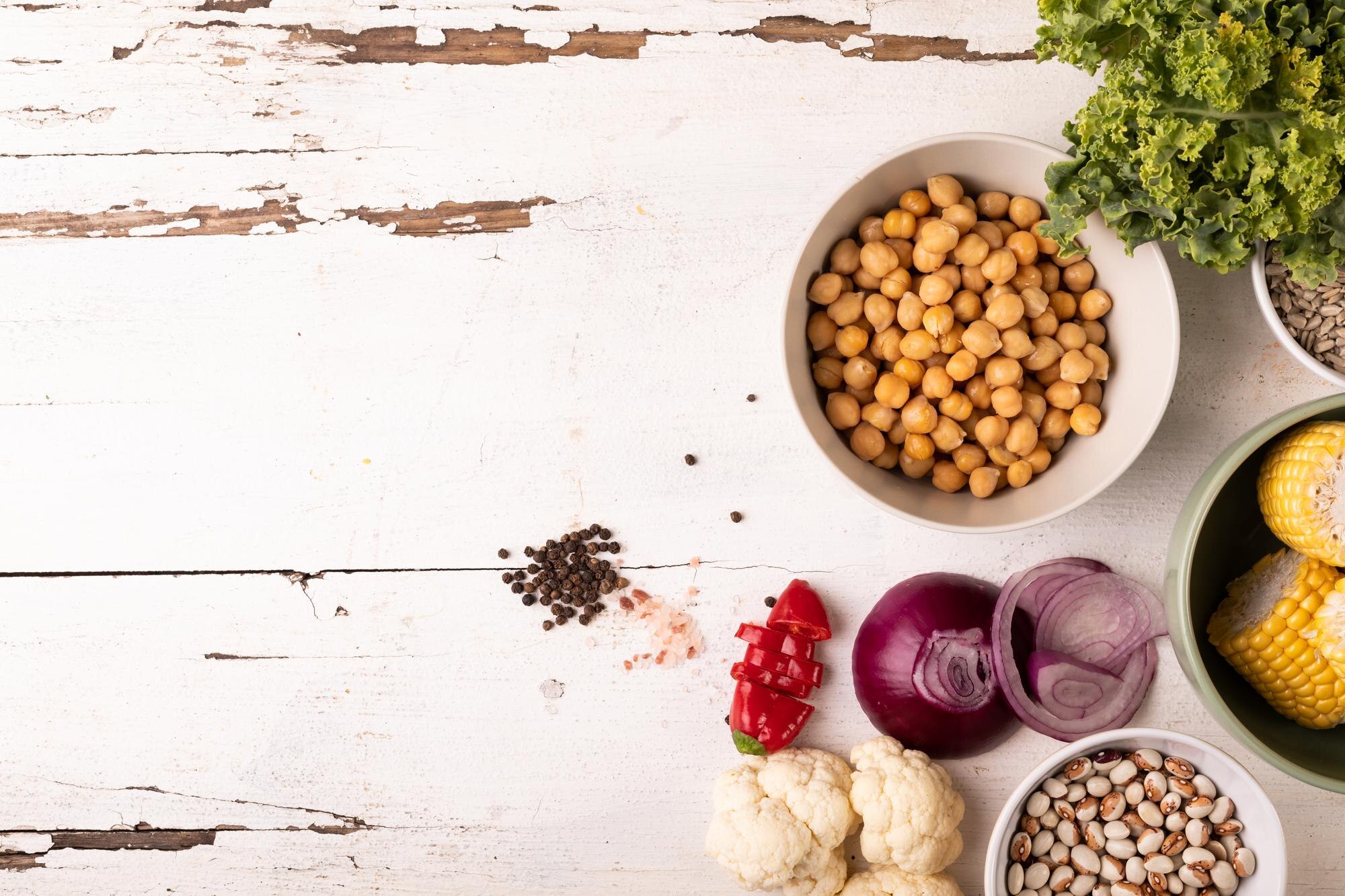 An overhead view of wholefood ingredients including vegetables, legumes, nuts, seeds and grains laid out on a light surface — foods often included in a fibre-rich, wholefood eating approach