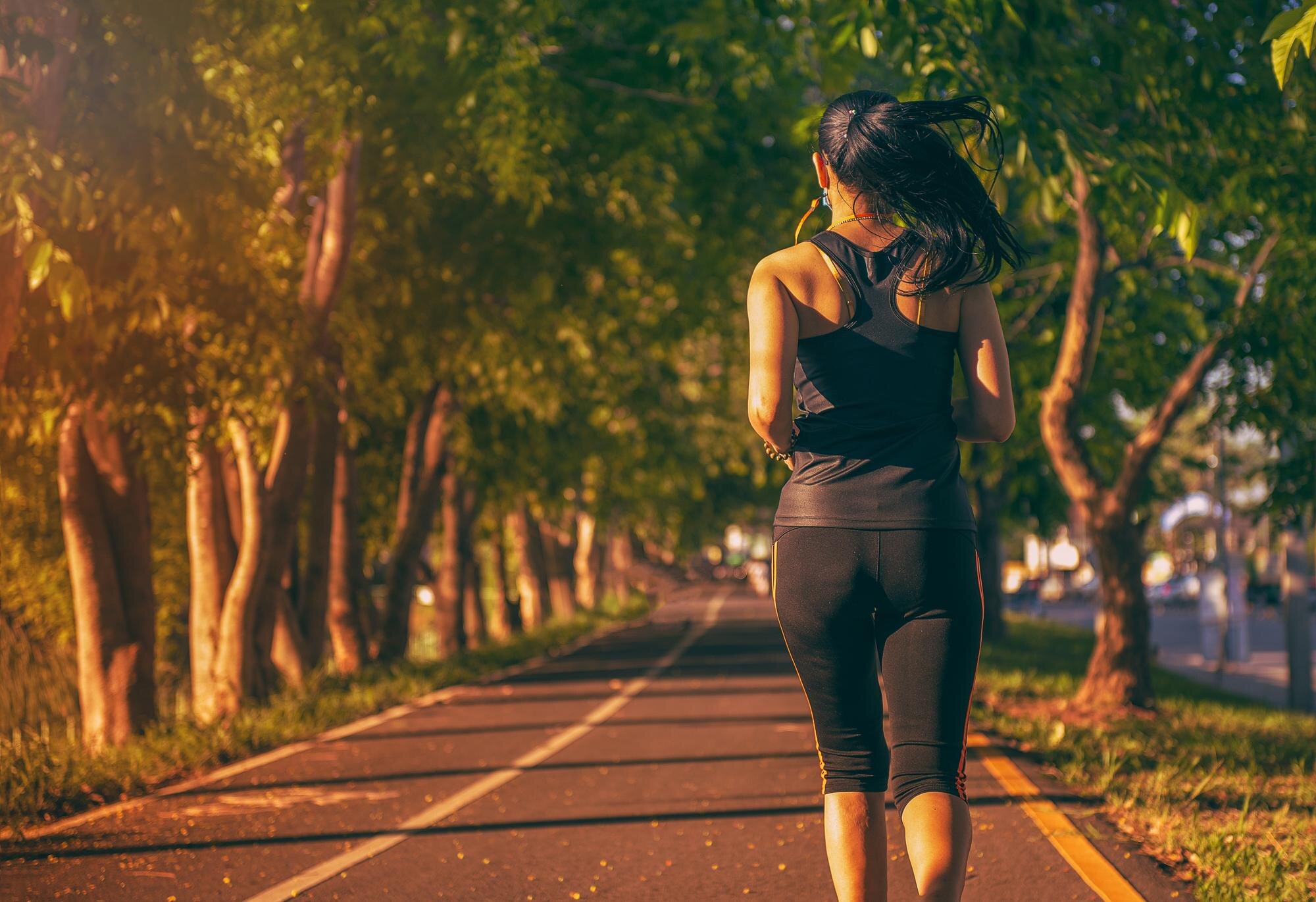 A woman jogging in a park surrounded by greenery — illustrating regular moderate-intensity aerobic activity as part of a healthy lifestyle